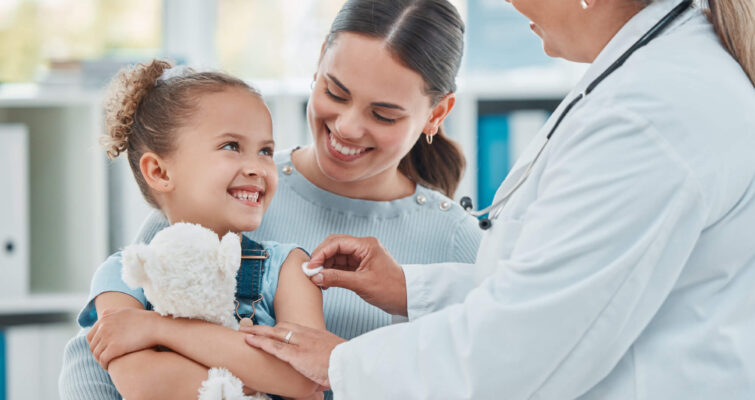 A woman holds a teddy bear while a doctor examines her, highlighting the theme of addressing missed diagnoses in children's health.