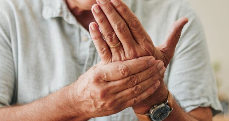 A man with arthritis holds his hands to his face, expressing discomfort related to osteomalacia and osteoporosis differences.