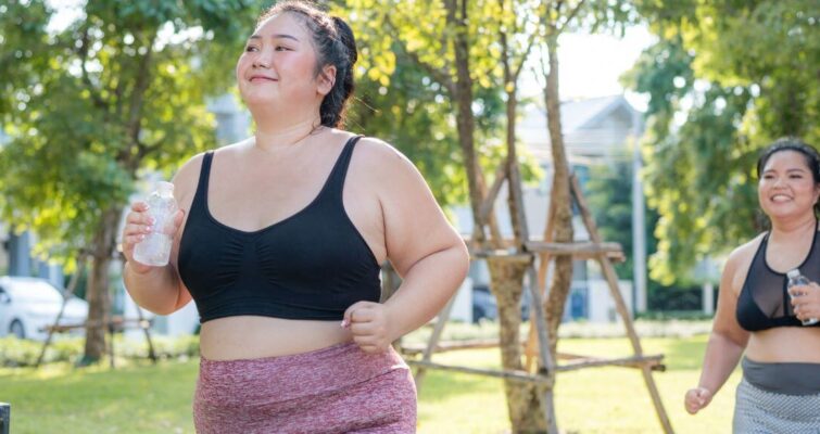 Two women in sports bras running together in a park, promoting fitness and well-being.
