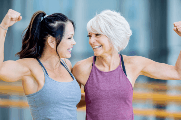 Two women flexing their muscles in a gym, showcasing strength and fitness.