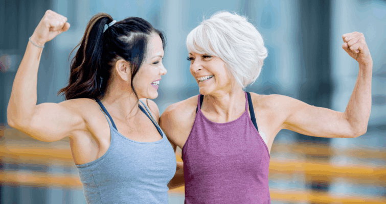 Two women flexing their muscles in a gym, promoting strength training for osteoporosis prevention and calcium supplementation.
