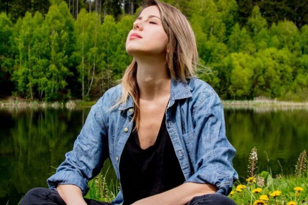A woman sitting on the grass by a serene lake, reflecting on the concept of Ojas in Ayurveda.