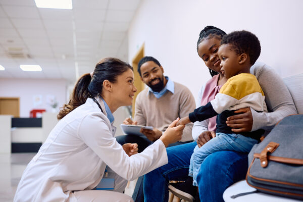 Smiling doctor holding hand of young child who came with parents for medical exam
