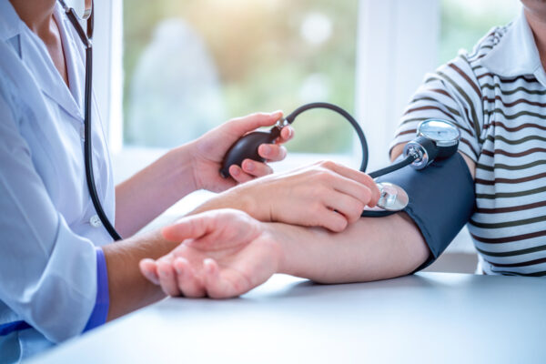A healthcare professional is measuring a patient’s blood pressure using a sphygmomanometer on their arm while seated at a table.