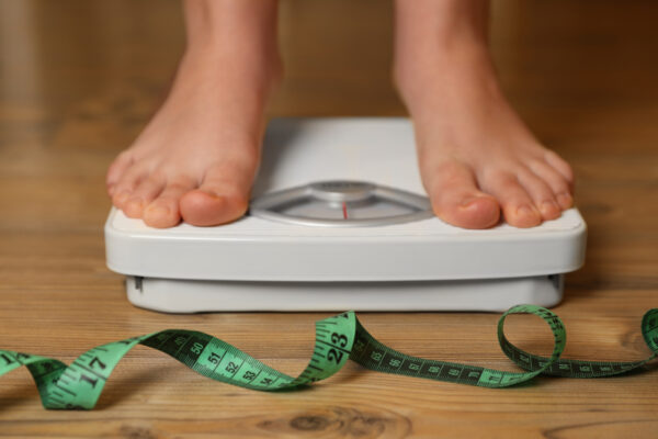 Person using scale near measuring tape on wooden floor, closeup