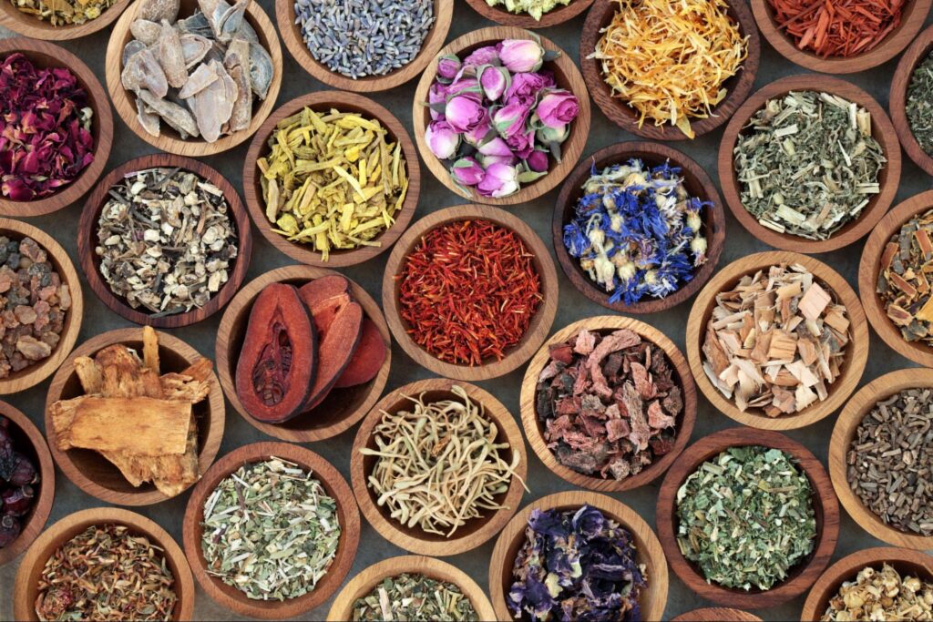 An overhead view of many wooden bowls full of colorful spices and herbs