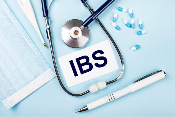 On a blue background, a stethoscope, a medical mask, pills, a pen and a white card with the text IBS Irritable Bowel Syndrome.