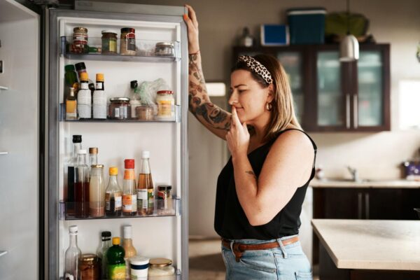 A woman looking in her refrigerator thinking