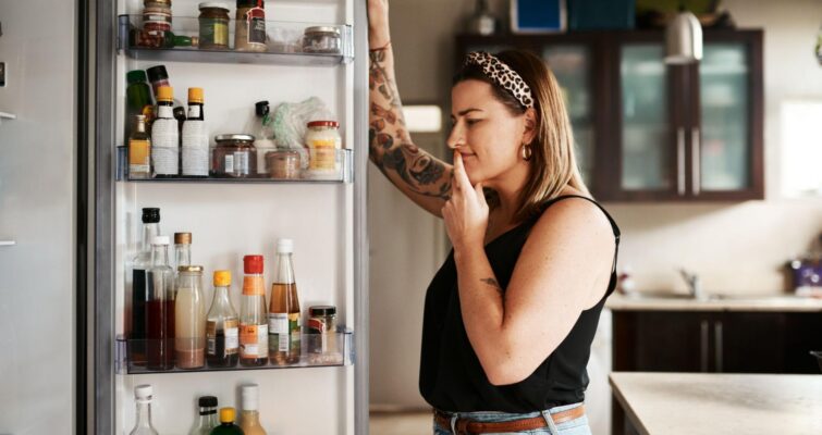 A woman looking in her refrigerator thinking