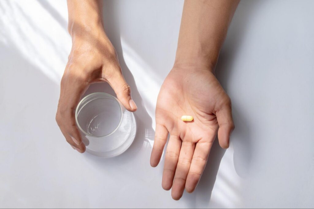 A close up of hands, one holding a pill and the other holding a glass of water
