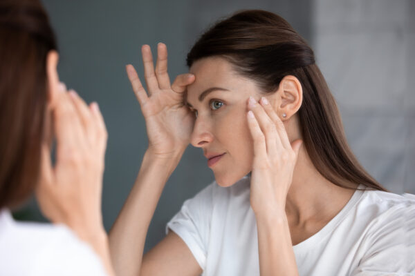 Close up of woman looking in mirror examining her aging skin