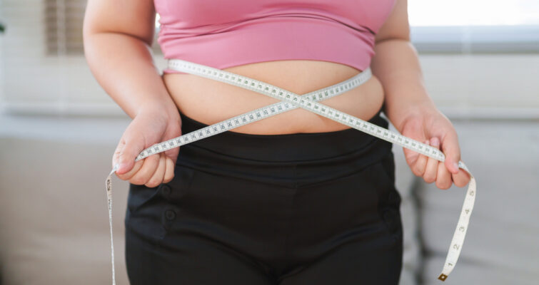 Close up overweight woman measuring her hip with tape measure.