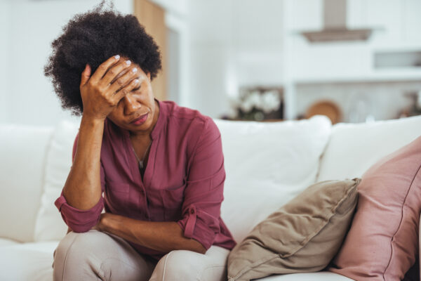 Fatigued Woman Sitting On Sofa Holding Head In Hand