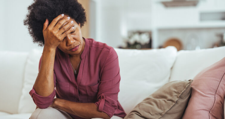 Fatigued Woman Sitting On Sofa Holding Head In Hand