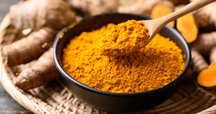 Turmeric powder in a bowl surrounded by fresh turmeric