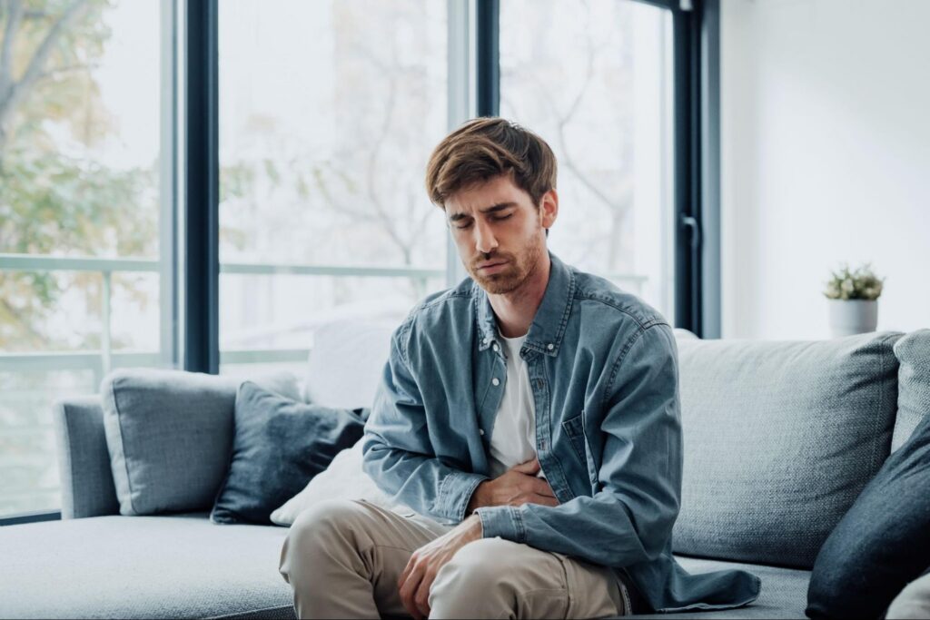 A man clutching his stomach sitting on a couch
