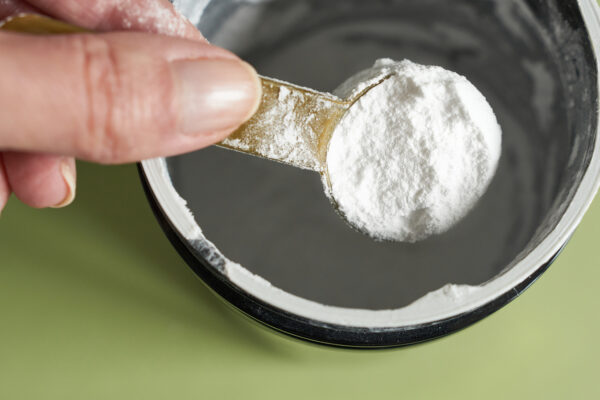 A spoonful of creatine powder in a metal jar, close-up.